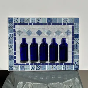 A unique hanging mosaic with a silver chain and five blue glass bottles ready for fresh or dried flowers.