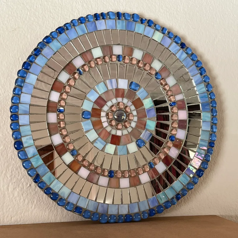 This flat, circular mosaic combines rings of mirror pieces and delicate tiles in clear blues and soft pinks, radiating outward beautifully.