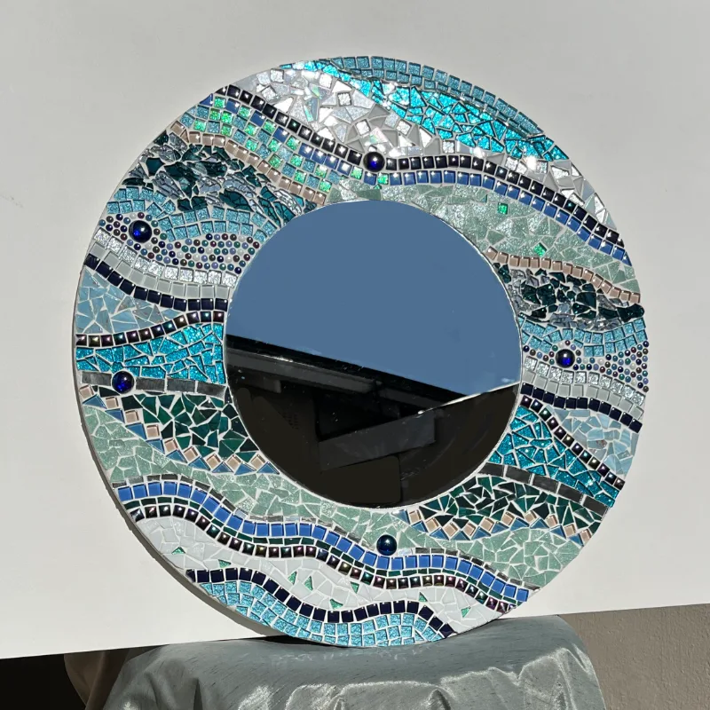 This large circular mirror features a broad mosaic frame in rippling shades of turquoise, blue, green, and teal.